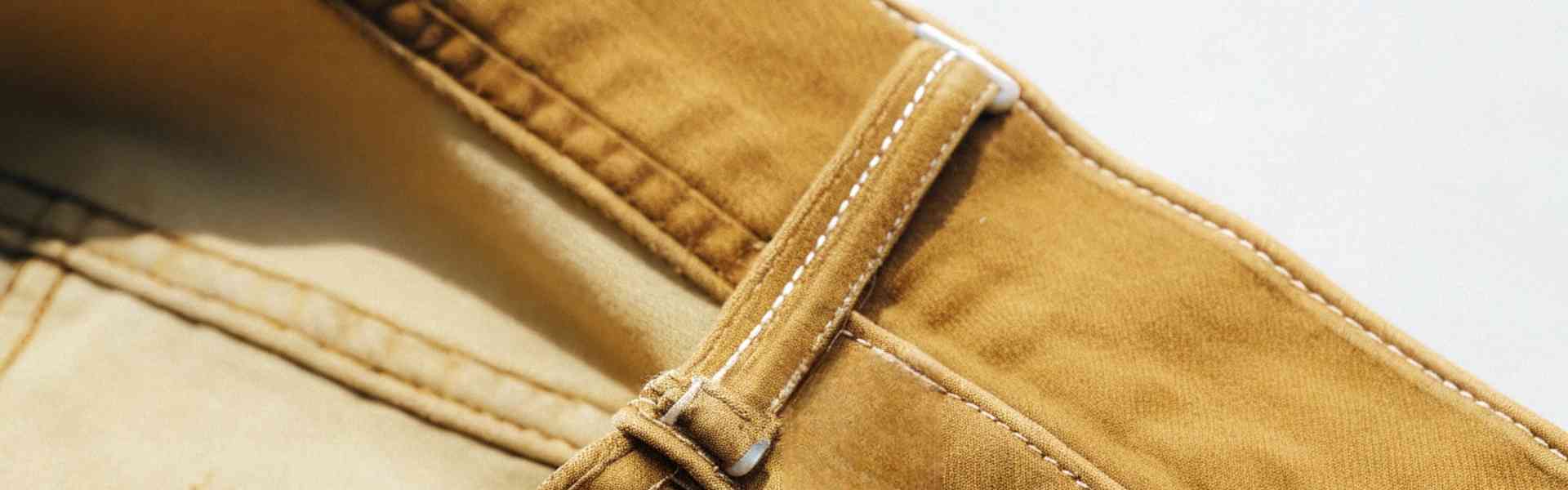 Detailed view of brown jeans with stitching and belt loop under sunlight.