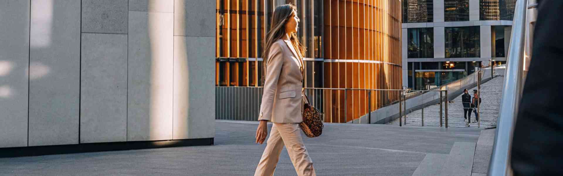 A stylish woman in a beige suit walking through a modern urban setting.