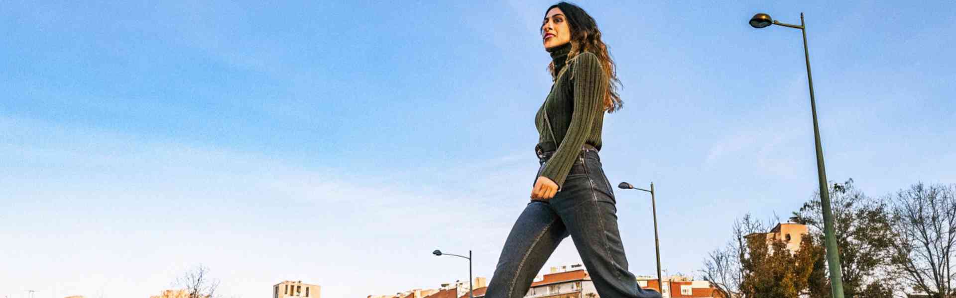 Stylish woman crossing the street in denim and white boots.