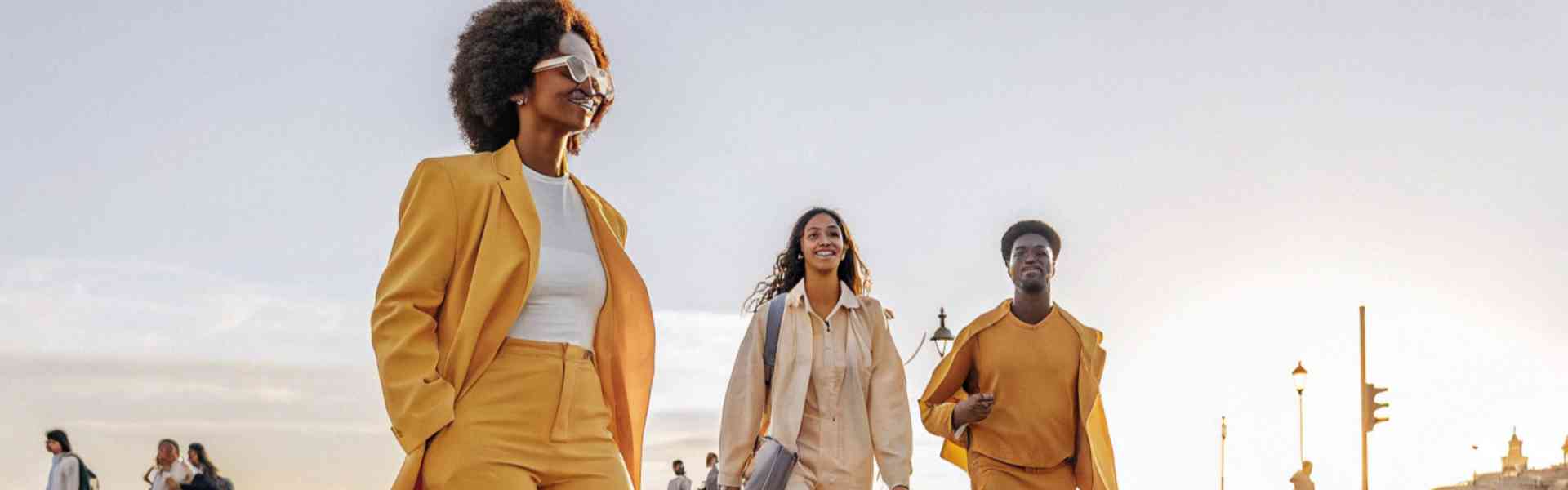 Three stylish friends in matching earth-tone outfits crossing a street at sunset.