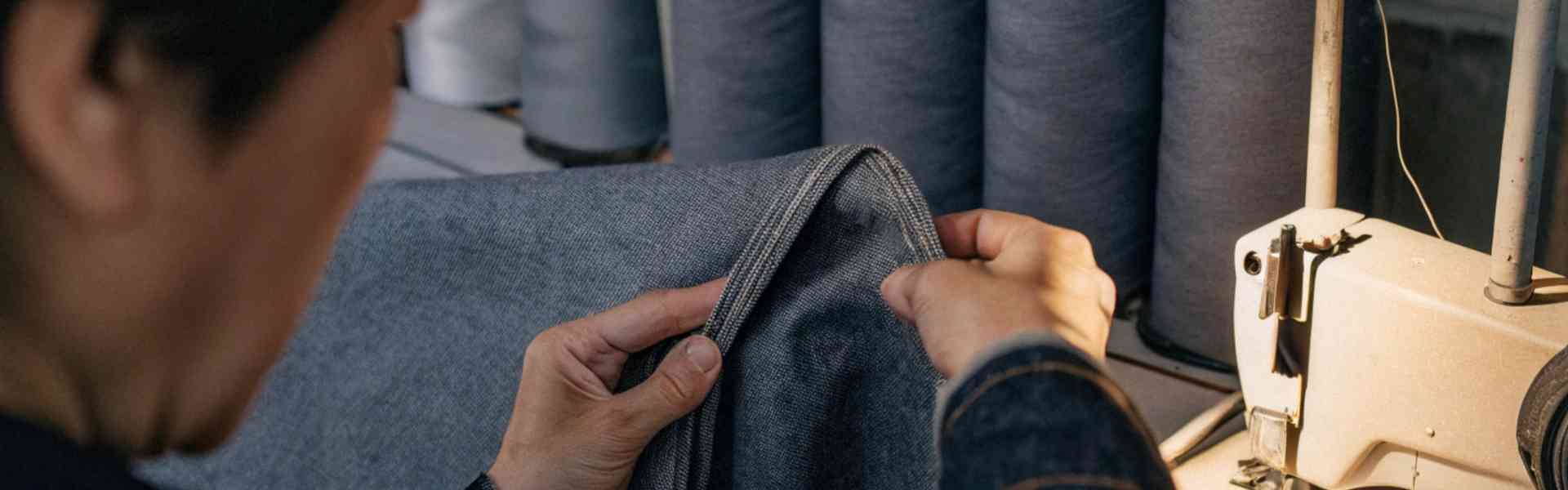 Worker examining denim fabric near sewing machine.