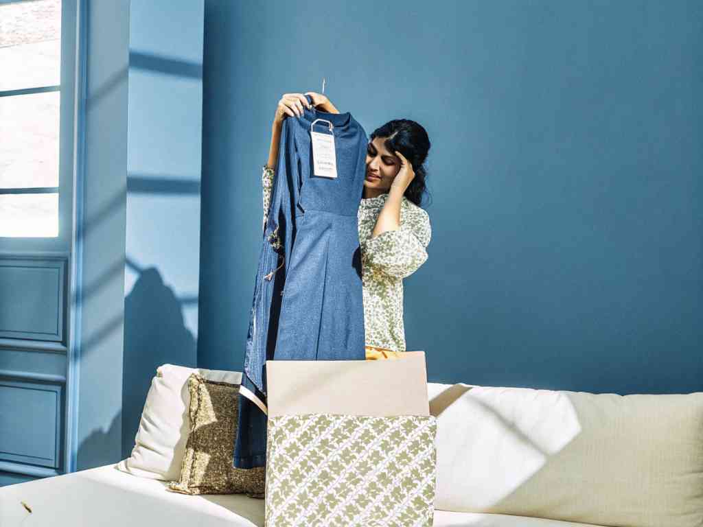 Woman looking at a blue dress from an opened package with concern.