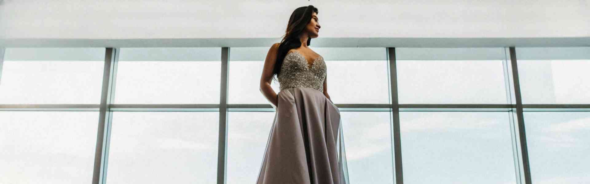 A woman in a sparkling ball gown standing under chandeliers.