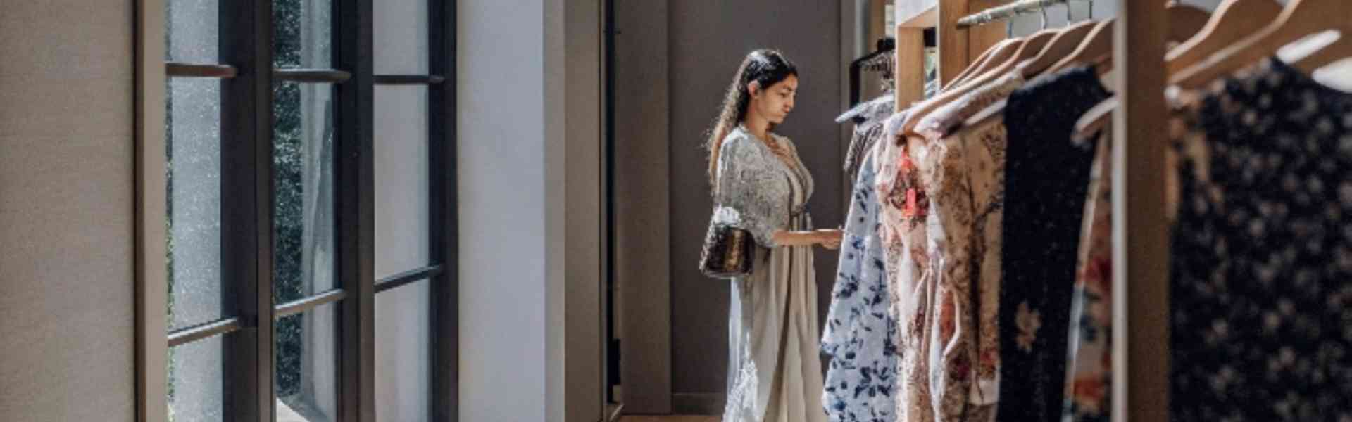 A woman browsing dresses in a sunlit boutique.