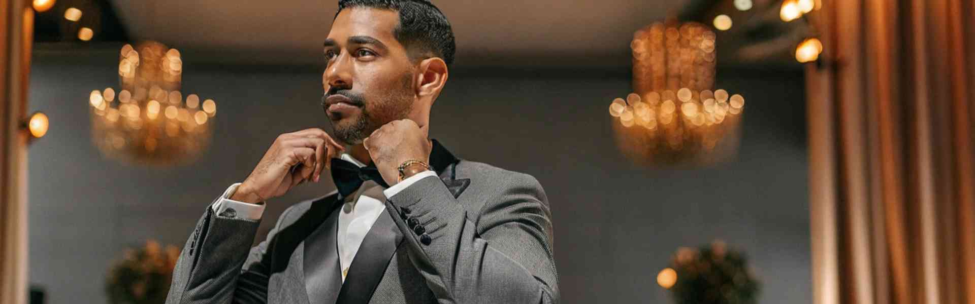 Man in a tuxedo adjusting his bow tie in a grand ballroom.