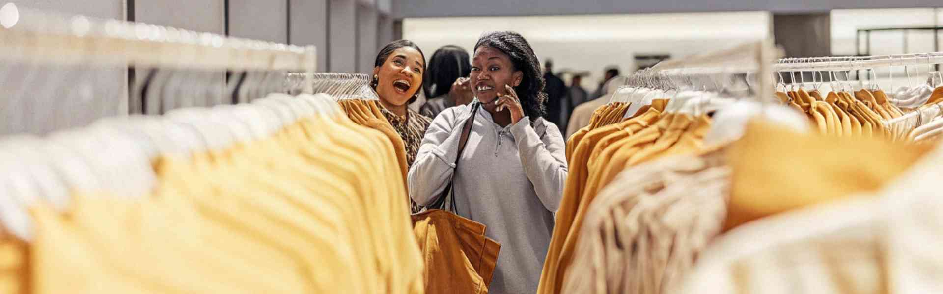 Two women happily browsing clothing racks in a fashion store.