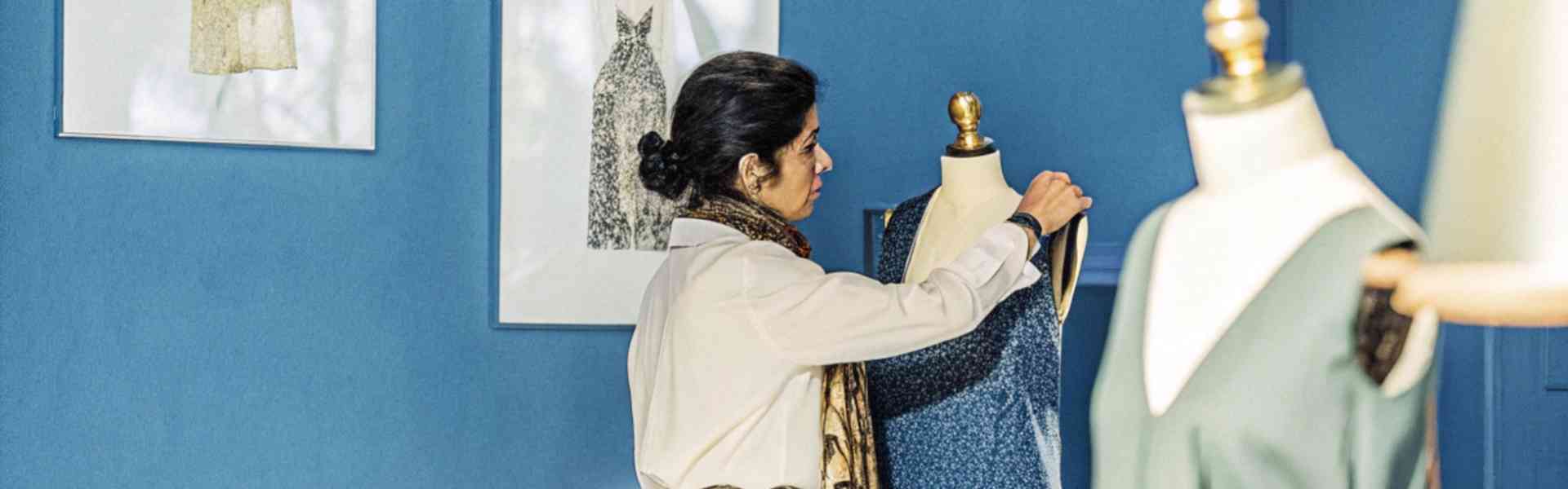 Fashion designer adjusting a dress on a mannequin in a blue studio.