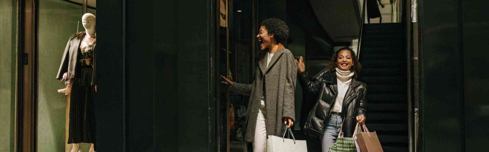 Two women excitedly leaving a store with shopping bags.