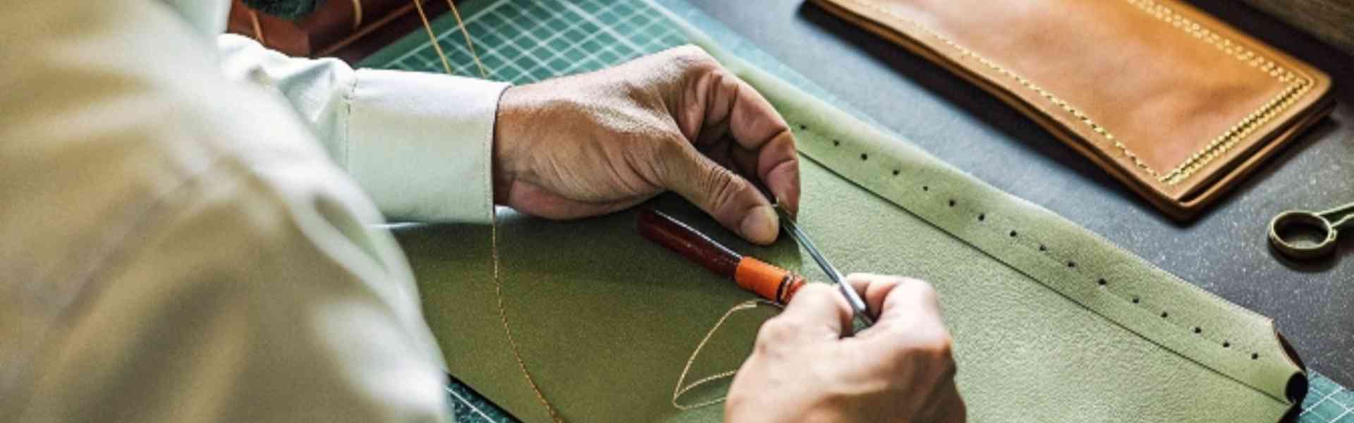 Artisan hand-stitching green leather with precision tools on a workbench.