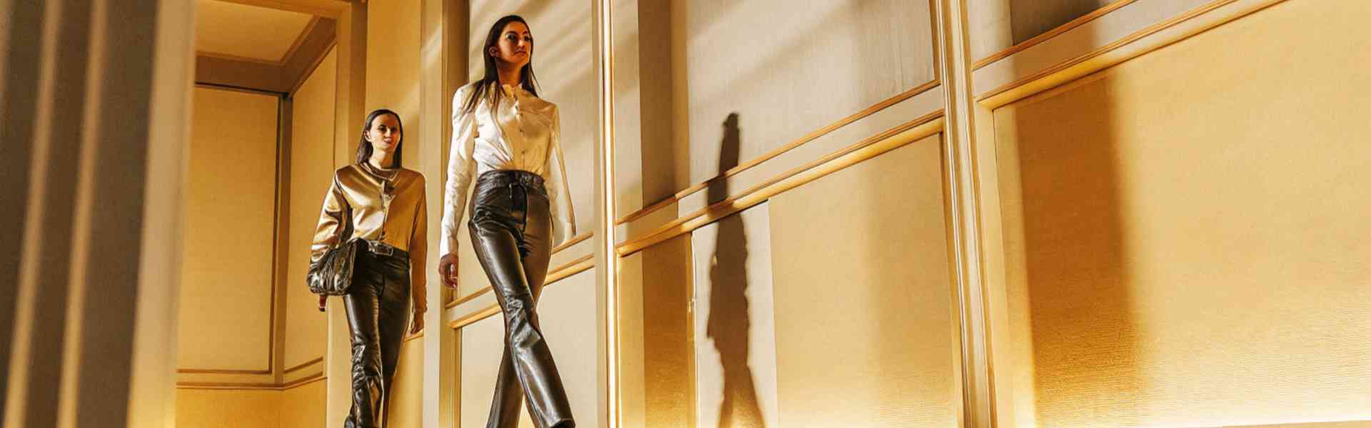 Two stylish women walking through a luxurious, golden-lit hallway.