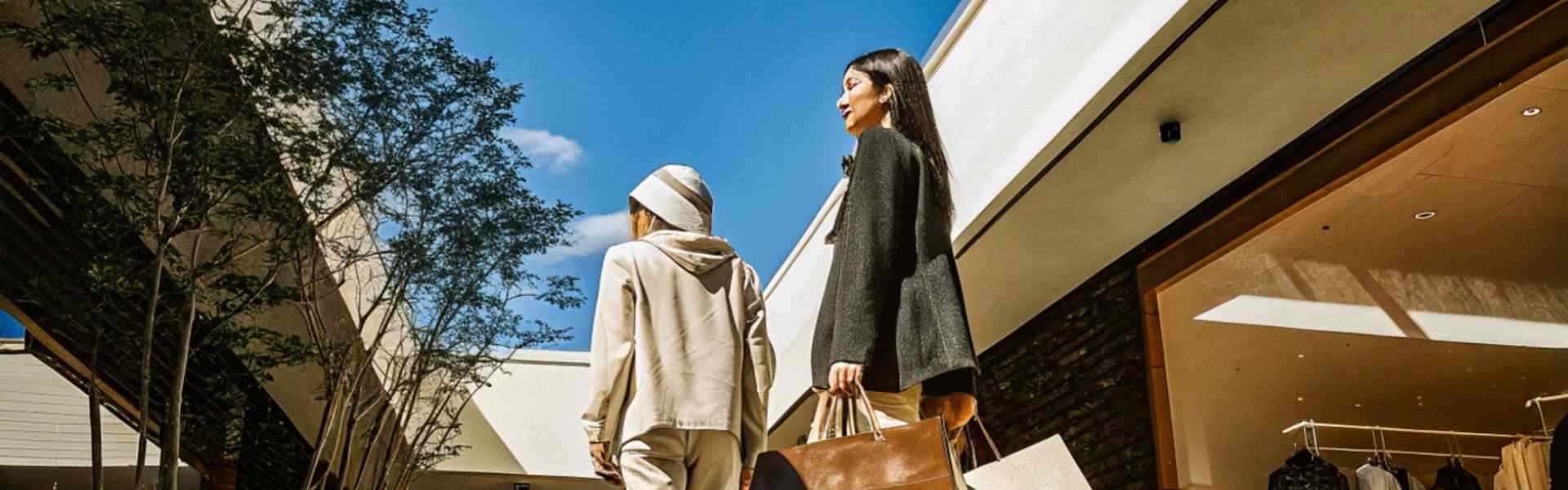 Two stylish women carrying shopping bags in an outdoor mall.