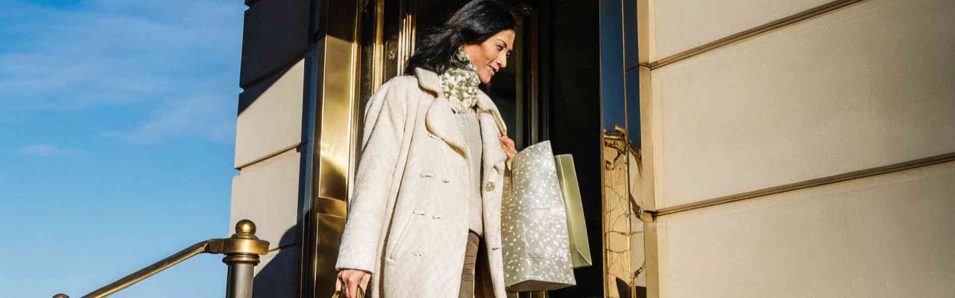 A stylish woman carrying shopping bags outside a high-end store.