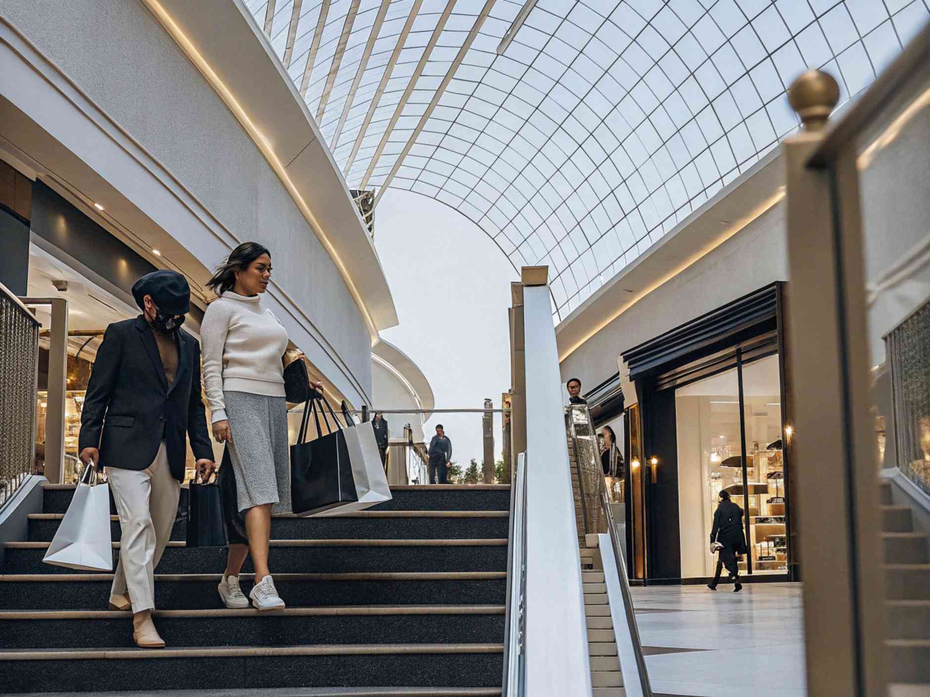 Two stylish women carrying multiple shopping bags in a modern mall.