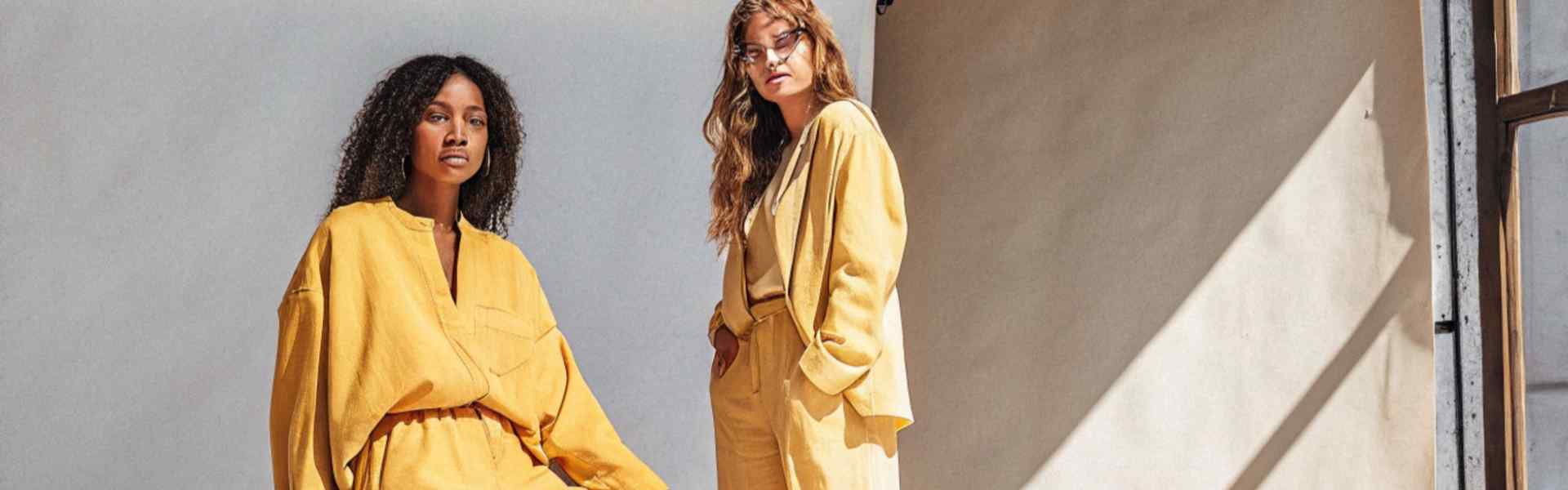 Two women in yellow outfits posing in a sunlit studio.