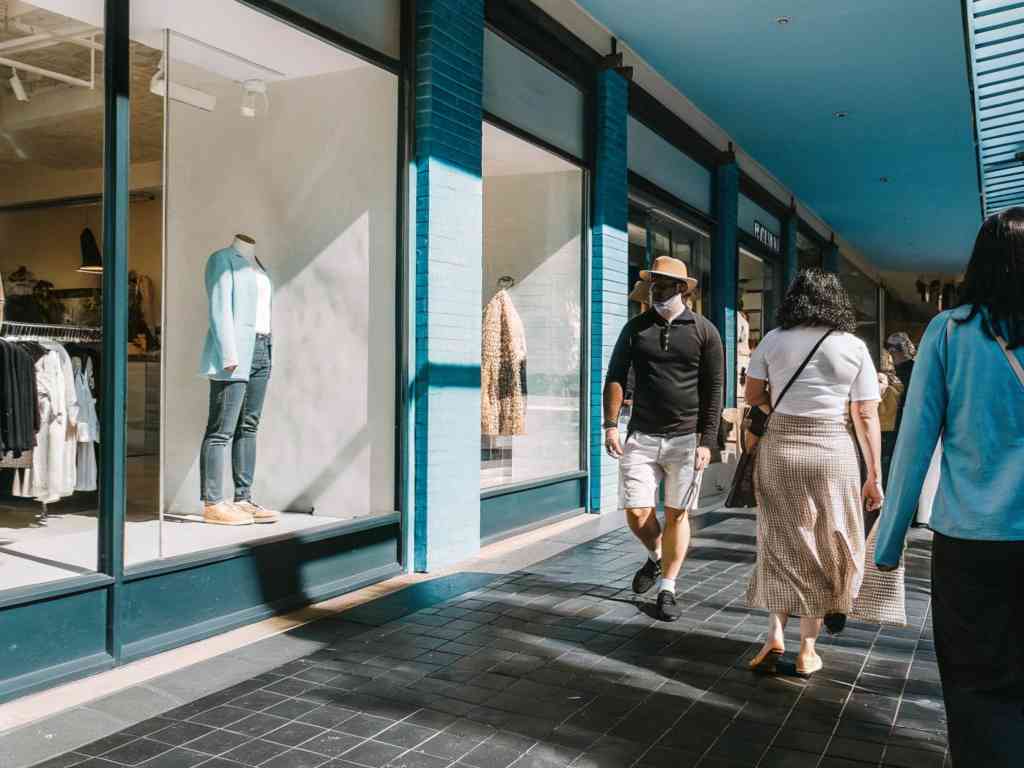 People walking past clothing store windows in a shopping district.