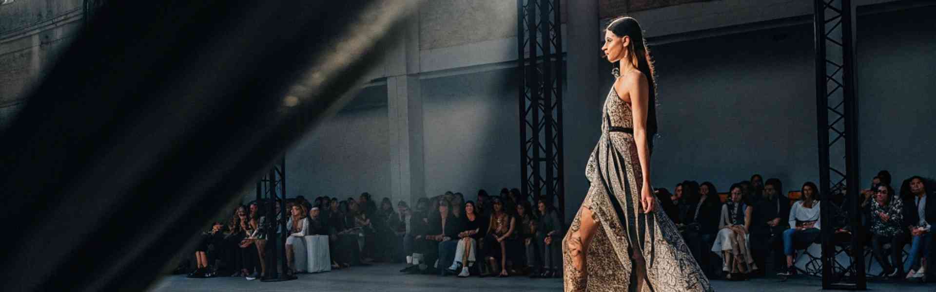 Model in a flowing gown walks down the runway at a fashion show.