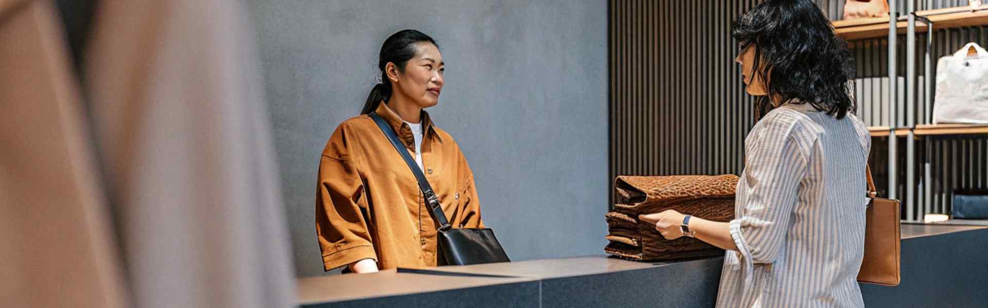 Customer and cashier in a clothing store with folded items at the counter.