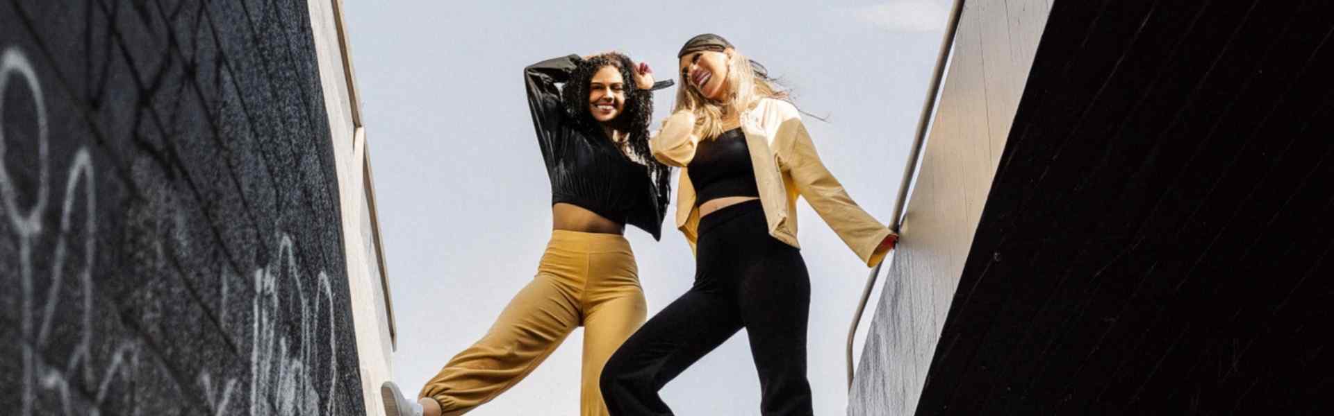 Two women posing in sporty outfits on an urban overpass.