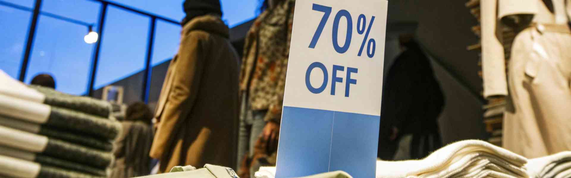 A 70% off discount sign in a clothing store with shoppers in the background.
