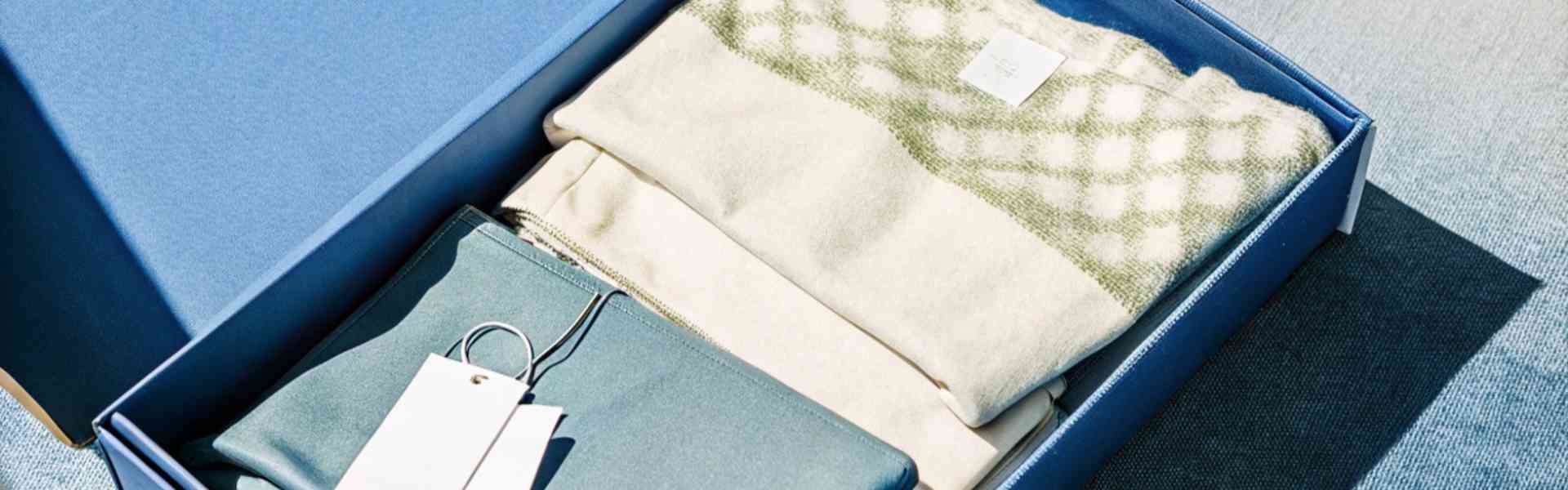 A blue gift box with a sweater and fabric neatly arranged inside