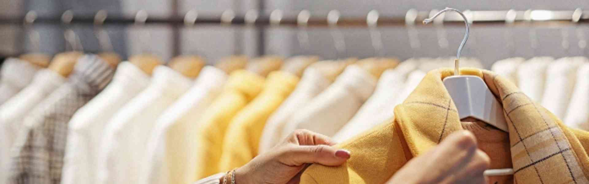 A person selecting a yellow plaid blazer from a clothing rack.