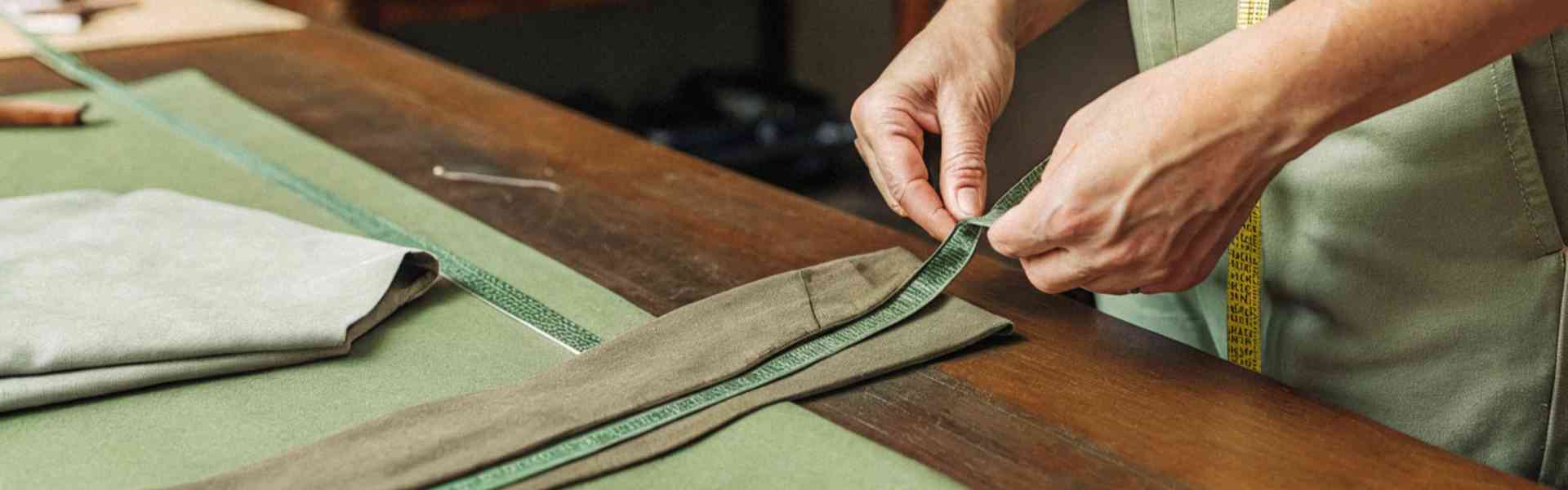 A tailor measuring and adjusting green fabric for clothing.