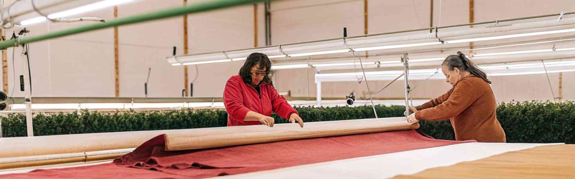 Two workers rolling out large fabric sheets in a factory.