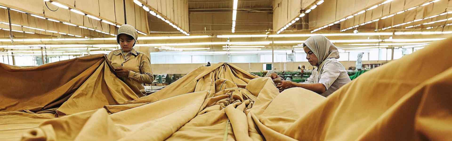 Workers handling large fabric sheets in a factory.