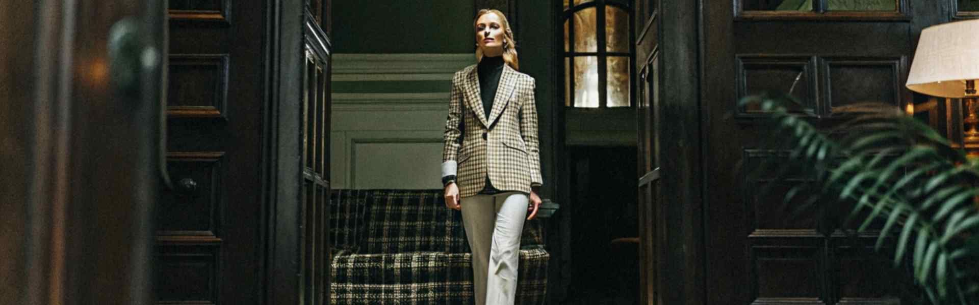 Woman in a checkered blazer walking through an elegant interior.