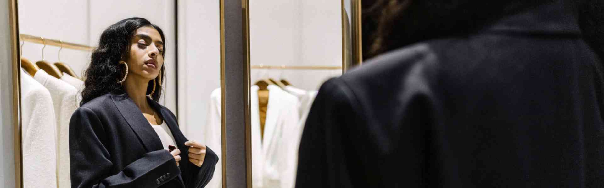 A woman in a black blazer checking her reflection in a stylish fitting room.