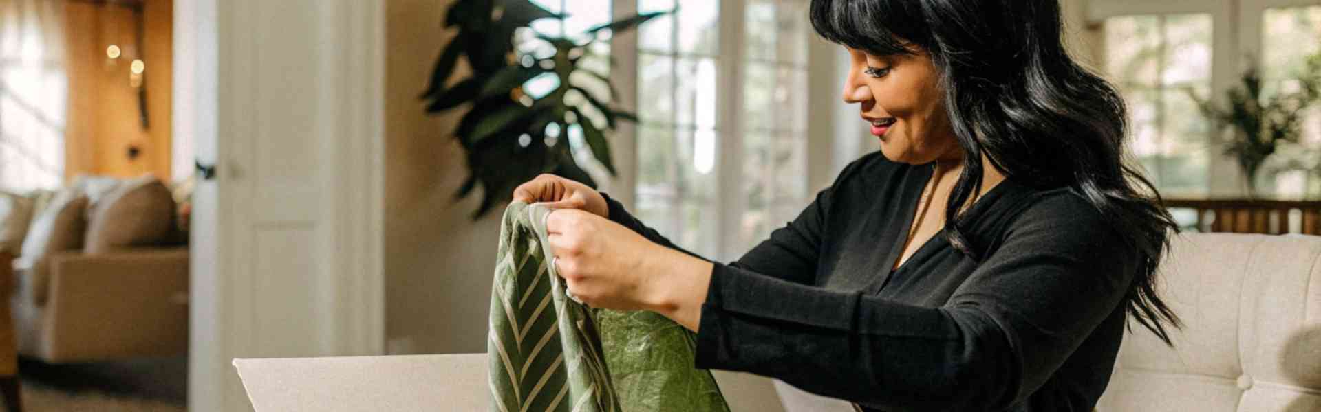 Woman opening a package and admiring a green dress at home.