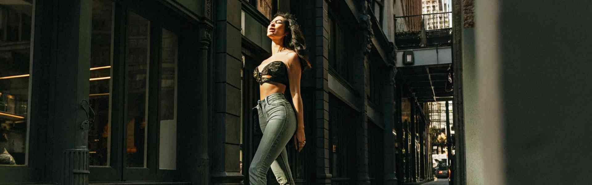 Stylish woman walking confidently in a city alley, wearing high-waisted jeans and heels.