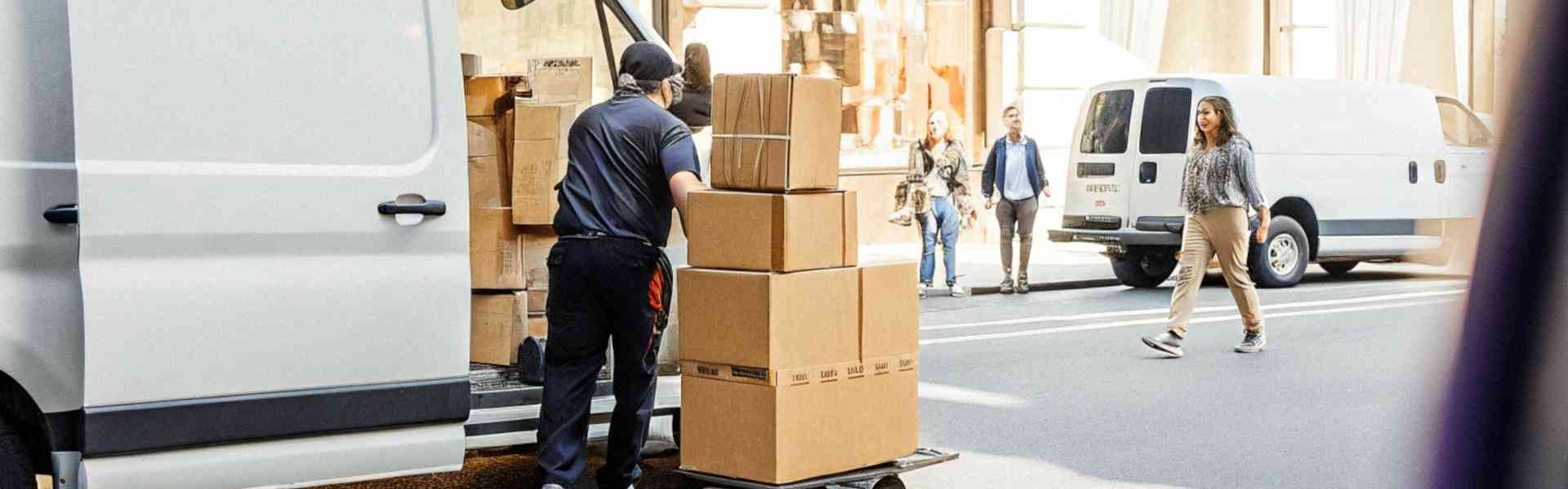 A worker unloading boxes from a van on a busy city street.