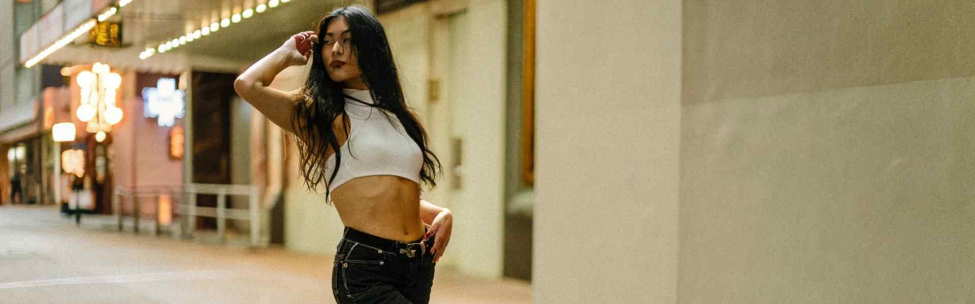 Woman posing in a city street wearing jeans and a white crop top.