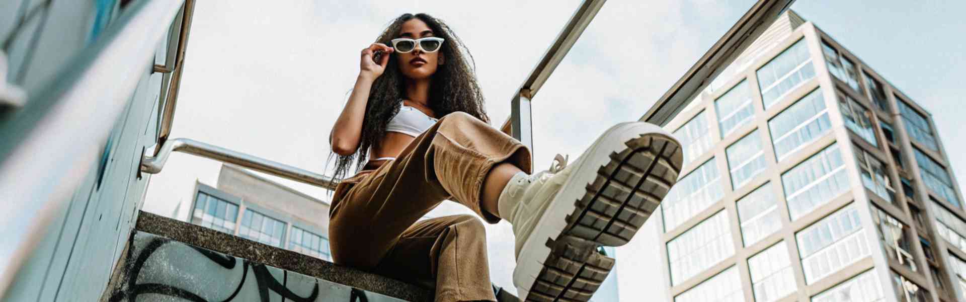 A stylish woman in sunglasses and chunky sneakers posing on a staircase.