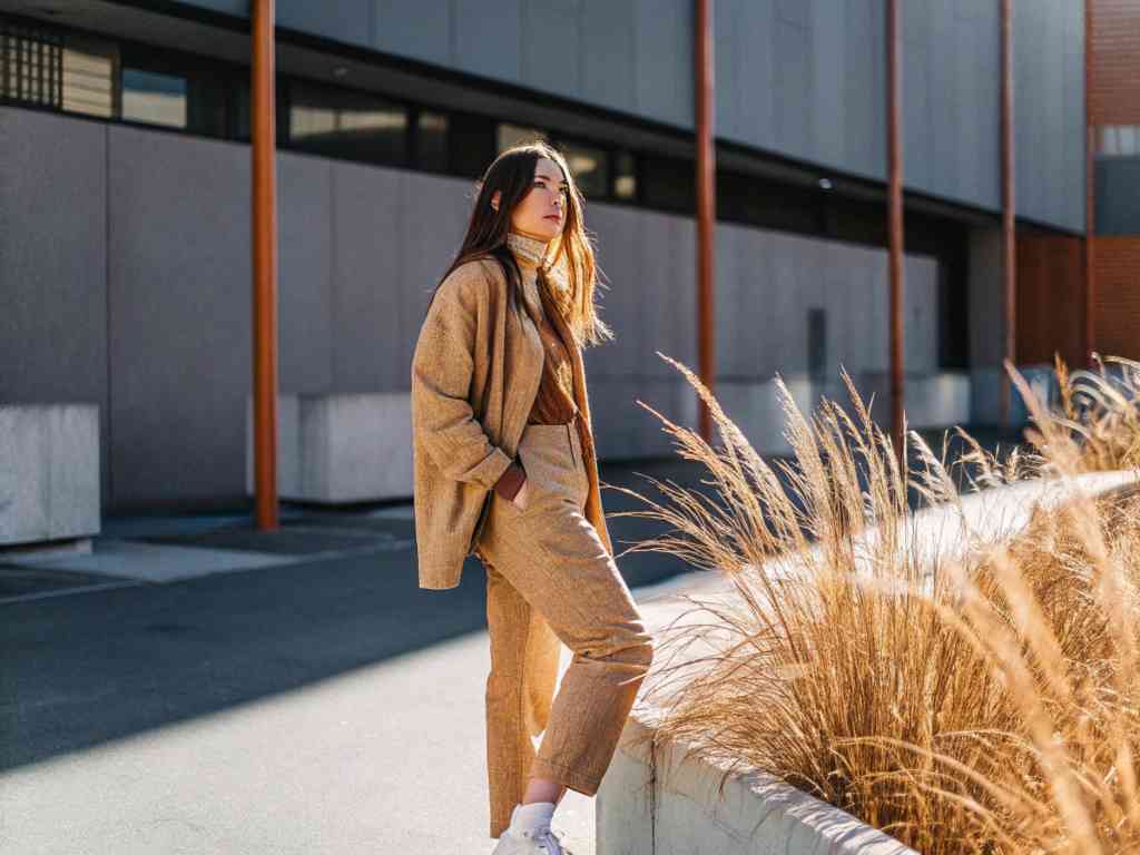 A stylish woman in a beige suit posing outdoors in sunlight.