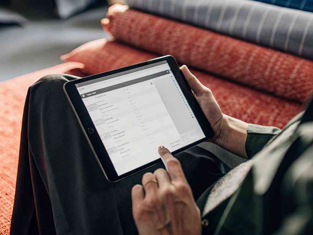 A person using a tablet to browse inventory or orders while sitting on fabric rolls.