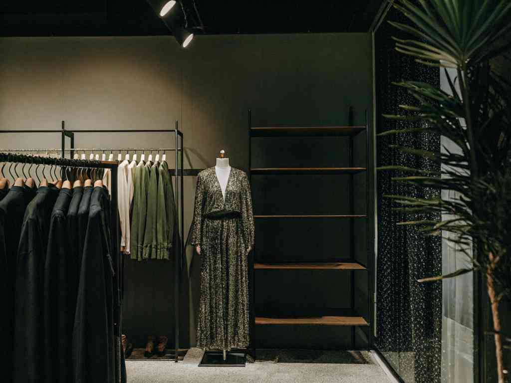 A fashion boutique with dark-toned clothing and mannequins in green dresses under warm lighting.