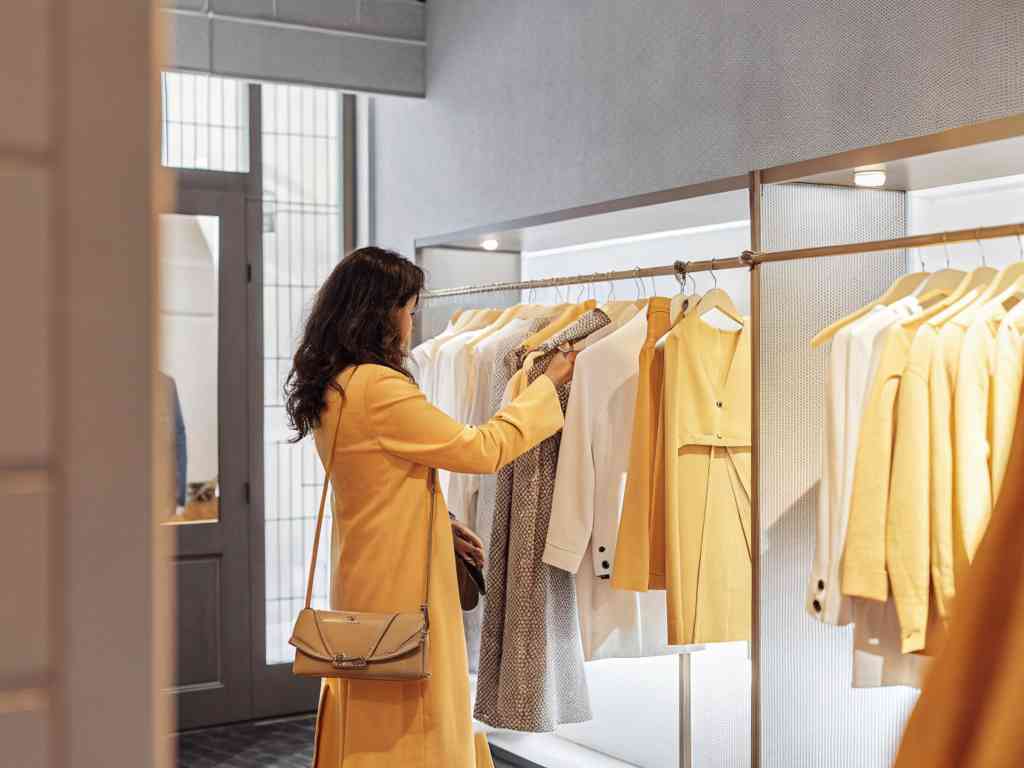 A woman in a yellow coat browsing a boutique clothing rack.