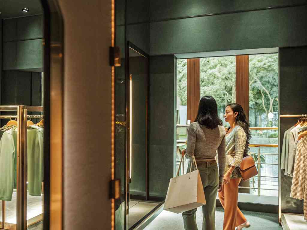 Two women shopping in a stylish clothing boutique with warm lighting.