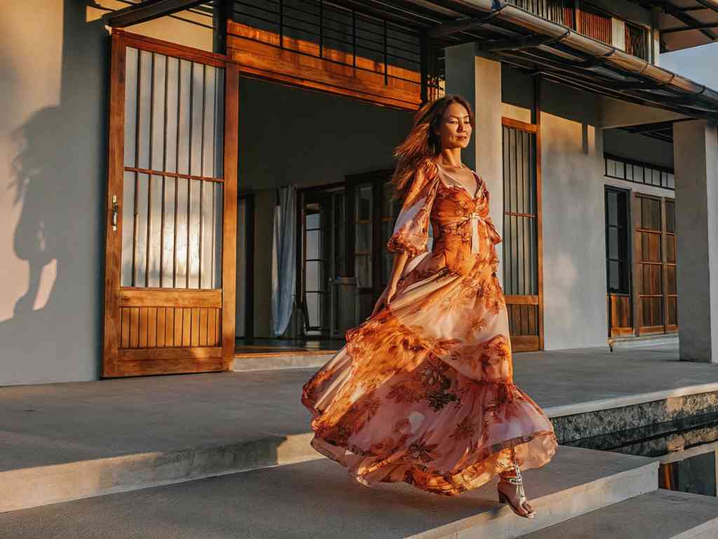 A woman in a flowing floral dress walking gracefully at sunset.