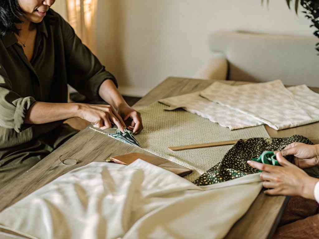 Two women working with fabric at a wooden table, cutting and preparing textile pieces.