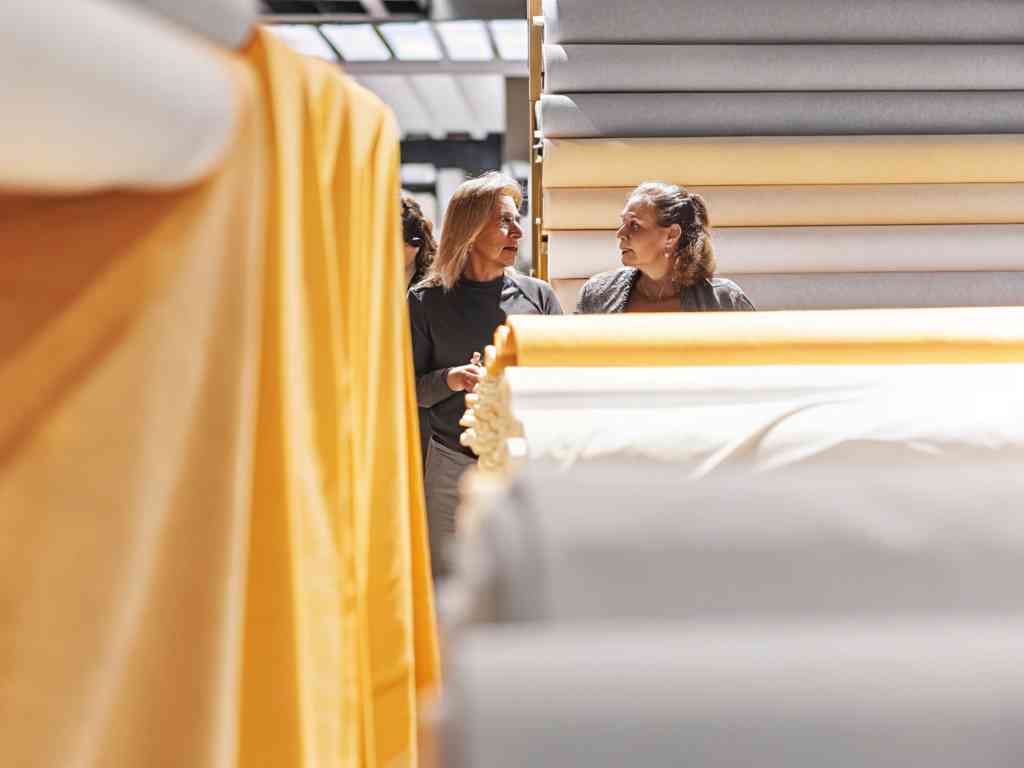 Two women browsing fabric rolls in a well-lit textile store.