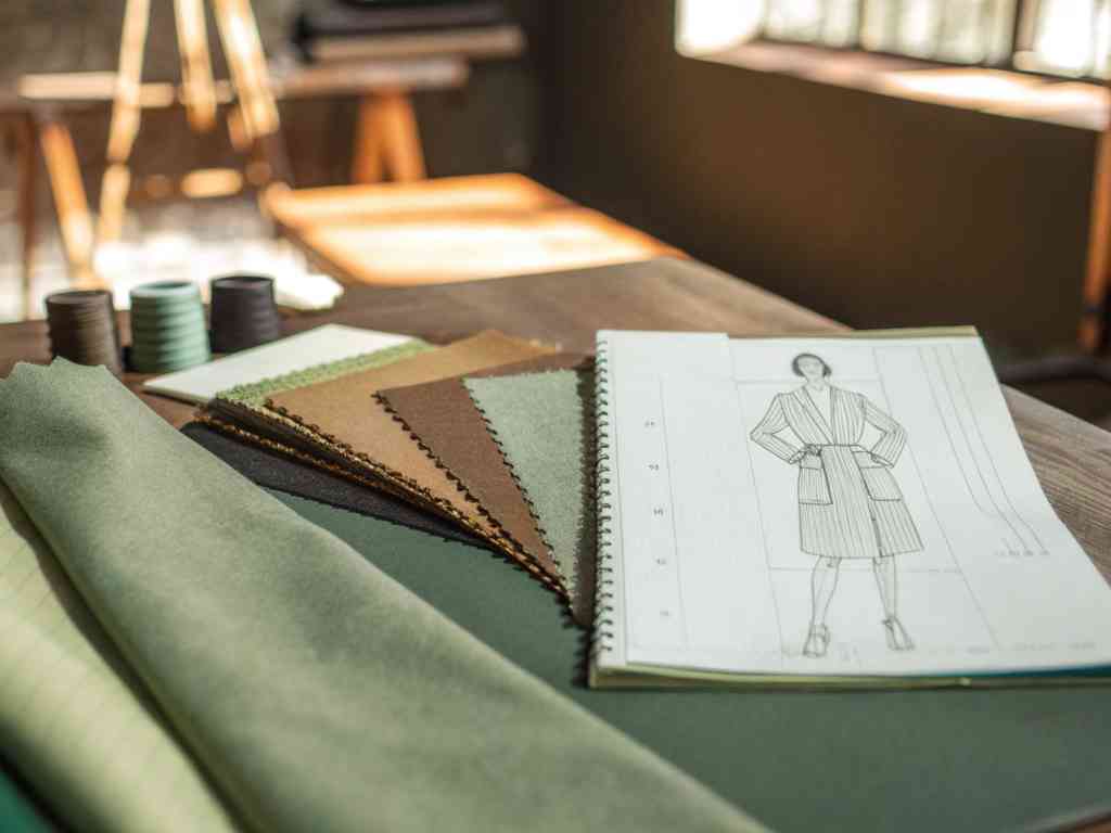 Fabric samples and a fashion sketchbook on a wooden table.