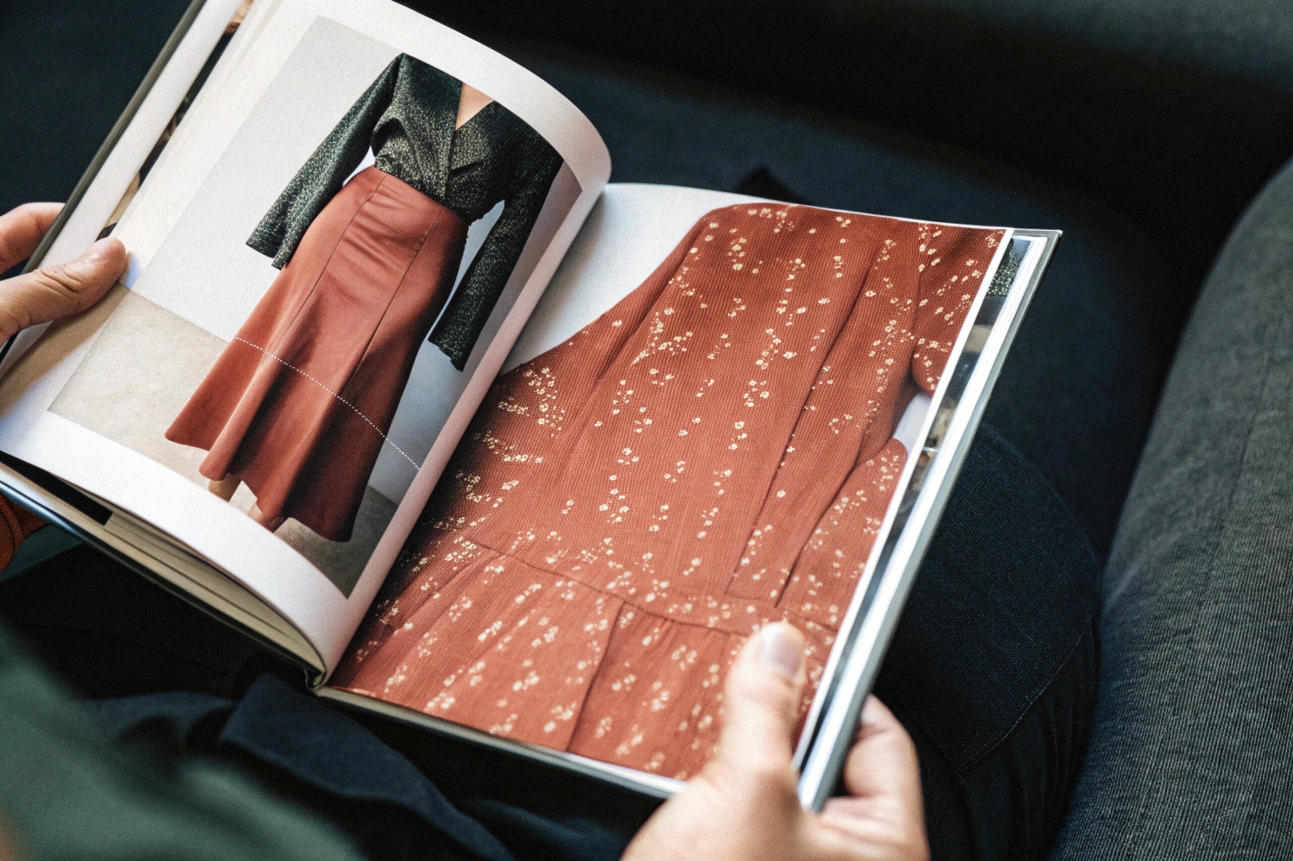 A person flipping through a fashion magazine featuring skirts and fabric details.