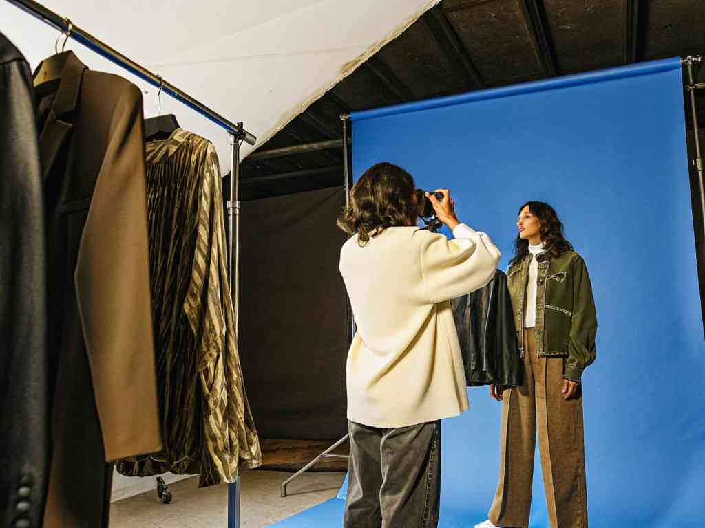 A photographer capturing a model against a blue backdrop in a studio.