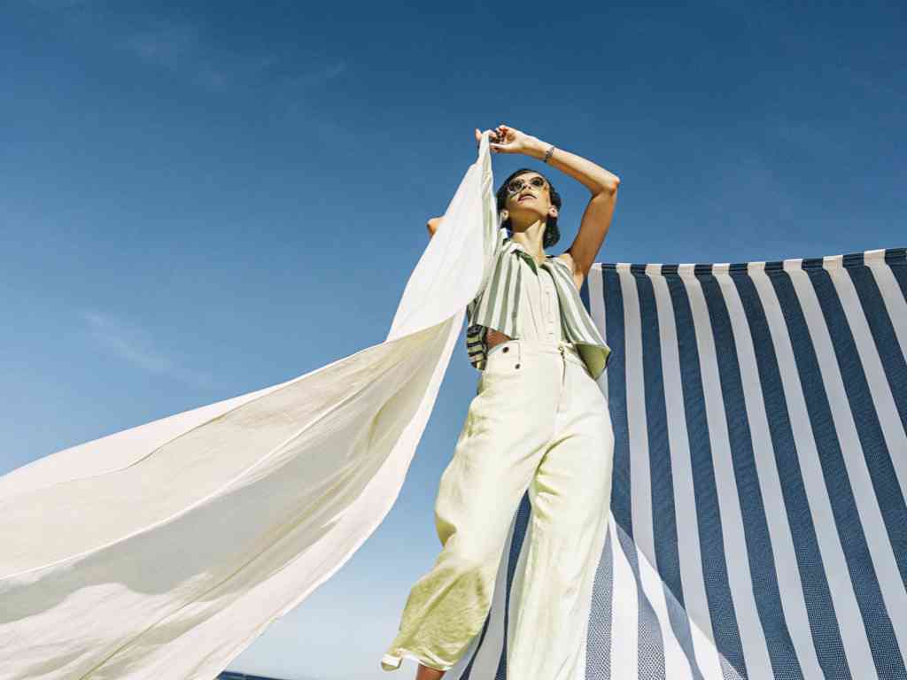 A stylish woman posing with flowing fabric against a blue sky.