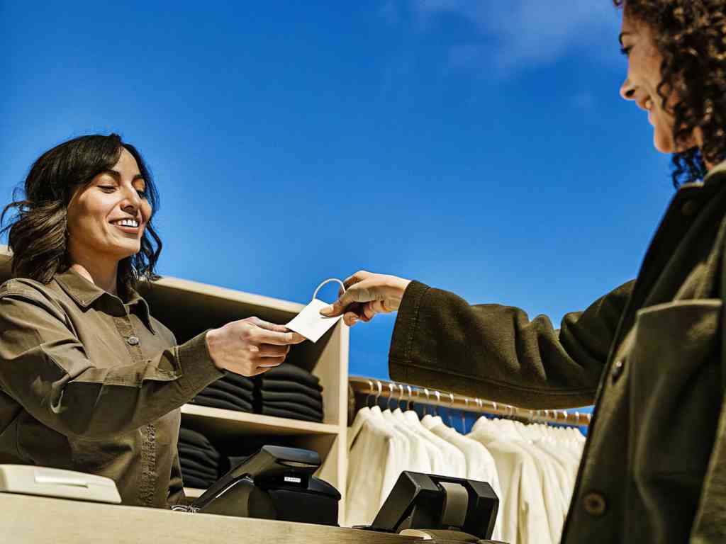 A smiling cashier hands a shopping bag to a customer.