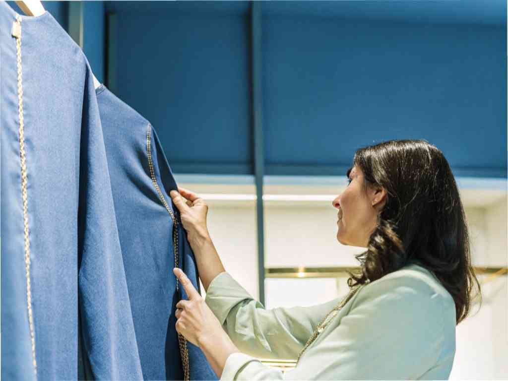 Woman inspecting blue garment on clothing rack.