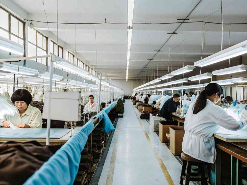 Workers in a brightly lit textile factory engaged in fabric inspection and sewing.